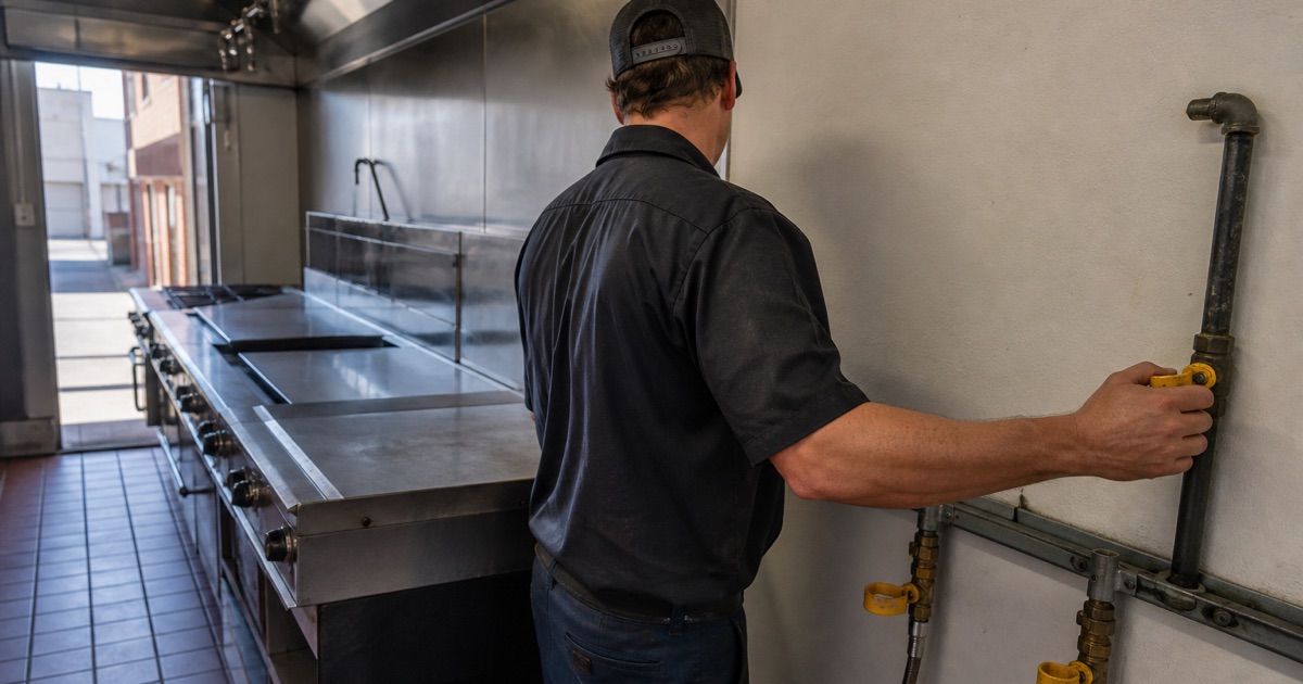 An installer working on gas piping behind a commercial cook line