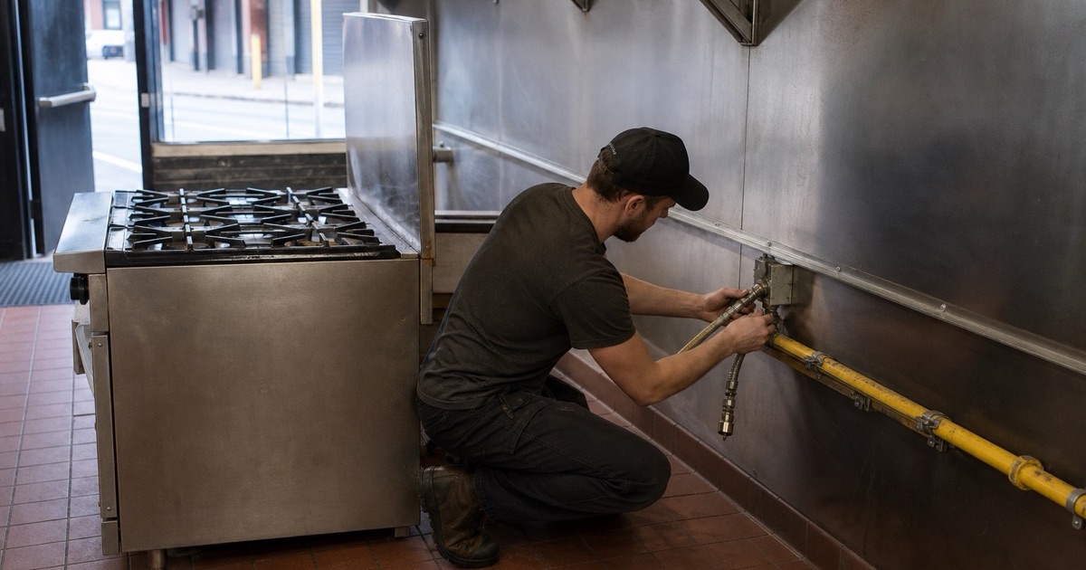 An installer connecting gas to a commercial range in a restaurant kitchen