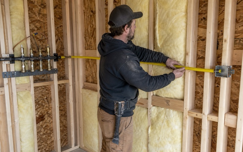 An installer routing new corrugated stainless steel tubing through drilled studs